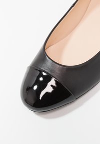 Ballerine in pelle nera con punta in vernice nera lucida. Il corpo è liscio e l'interno è di un beige chiaro in contrasto con il colore esterno.