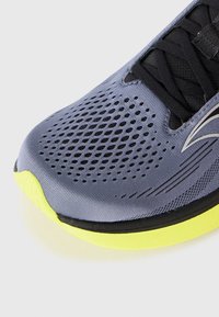 Running shoe with a grey upper featuring mesh detailing, black accents, and a bright yellow sole. Includes laces and streamlined design.