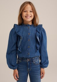 Modrá džínsová blůza s volánkovým límcem, koulemi rukávů a dřevěnými knoflíky, v kombinaci s modrými džíny pro sladěný vzhled.