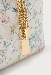 Bolso con estampado floral en crema, con detalles en cadena dorada y un cierre. El material parece texturizado con detalles metálicos.