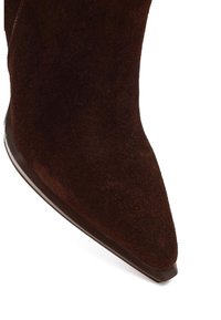 Bota de tobillo de ante marrón con punta puntiaguda y suela lisa oscura. La parte superior presenta una textura suave y una silueta elegante.