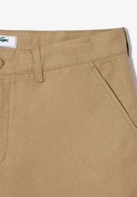 Pantaloni in cotone khaki con una texture liscia, dotati di una vita standard, chiusura con bottone e tasche laterali inclinate.