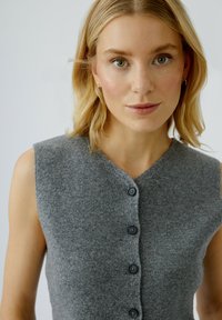 Grauer, gestrickter Pullunder mit V-Ausschnitt, ärmellosem Design und fünf schwarzen Knöpfen auf der Vorderseite. Weiche Textur mit einem gerippten Muster.