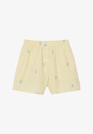 Bóxers a rayas amarillas con ilustraciones de jugadores de tenis en azul y bragueta con botones bajo una cintura elástica.