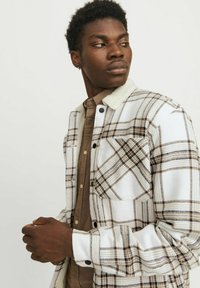Geruite shirtjas met witte en bruine tinten, knoopsluiting en fluffy witte kraag. Inclusief een voorzak en een contrasterend bruin shirt eronder.