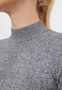 Szary sweter z prążkowanym wysokim kołnierzem, wykonany z teksturowanego dzianiny o przylegającym kroju, idealny do warstwowego ubierania się w chłodniejsze dni.