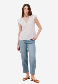 Blusa bianca a maniche corte e scollo a V con maniche arricciate; abbinata a jeans dritti azzurri e sandali marroni con strap.