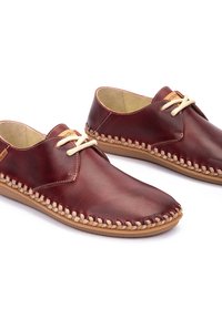 Zapatos de cuero marrón con una forma redondeada, costuras beige alrededor de la suela y cordones crema. Presentan una textura suave y un diseño minimalista.