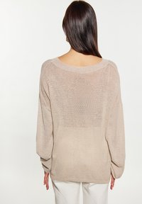 Pulover oversized bej cu decolteu larg, mâneci balon și textură transparentă, având un tiv din spate ușor alungit.