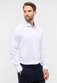 Weißes Langarmhemd mit Button-Down-Kragen, ausgestattet mit einer Tasche und einem kontrastierenden, gemusterten inneren Kragen. Glatte Stofftextur.