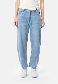 Jeans de mezclilla azul claro con un corte holgado, que presentan un sutil patrón geométrico y un diseño estándar de cinco bolsillos. Combinados con zapatillas blancas.