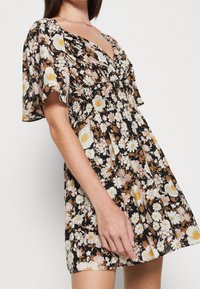 Schwarzes Blumenkleid mit kurzen, flatternden Ärmeln. Das Muster zeigt weiße, rosa und gelbe Blumen. V-Ausschnitt, geraffte Taille, leichter Stoff.