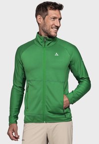 Grüne Reißverschlussjacke aus strukturiertem Material mit hohem Kragen, geripptem Design, seitlichen Taschen und einem kleinen Logo auf der Brust.