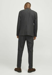 Dunkelgrauer Anzug mit einem maßgeschneiderten Blazer und schmal zulaufenden Hosen, die eine glatte Textur und ein dezentes Webmuster aufweisen, ergänzt durch braune Schuhe.