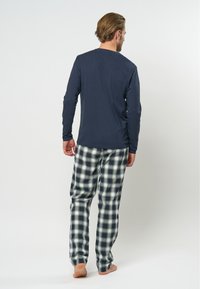 Marineblauw langemouwen top gecombineerd met groen-witte geruite pyjamabroek. Zachte stof, ontspannen pasvorm, subtiele halslijn en elastische tailleband.