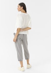 White knit sweater with a loose fit and short sleeves paired with gray and white striped cropped pants and beige sneakers.