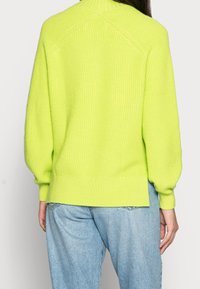 Neon-grüner Strickpullover mit geripptem Muster, hoher Kragen und leicht überschnittenen Ärmeln. Mit geradem Saum abgeschlossen.
