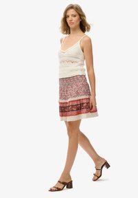 Biała dzianinowa bluzka na ramiączkach z misternymi wzorami, zestawiona z szortami w kwiatowy wzór, ozdobionymi koronkowym wykończeniem i kolorowymi poziomymi paskami. Brązowe sandały na obcasie.