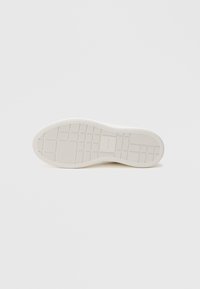 Λευκή καουτσούκ σόλα παπουτσιού με υφές και σχηματικές ρακές και πλέγμα. Λείος περιφερειακός χώρος και ελαφριά καμπύλη στην περιοχή της φτέρνας.