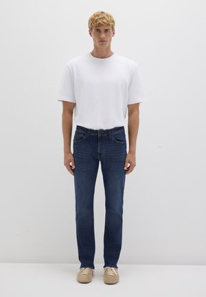 Men's outfit featuring a plain white cotton T-shirt, dark blue denim jeans with a straight cut, and beige sneakers. Simple design and classic colors.