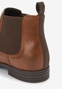 Brown leather ankle boot with elastic side panels, rounded toe, and textured brown rubber sole. Features a tab at the back for easy wear.