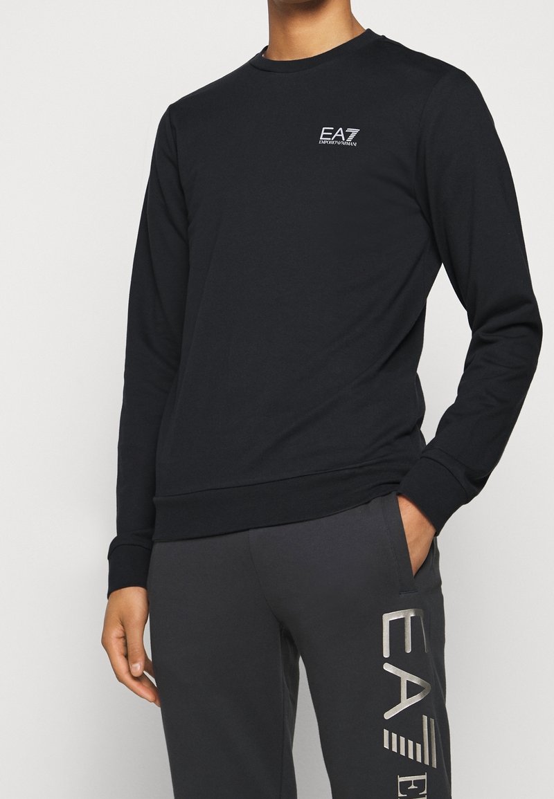 Felpa nera a maniche lunghe in cotone, con scollo rotondo e piccolo logo bianco sul petto a sinistra. Tessuto liscio.