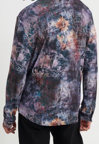 Camicia a maniche lunghe con stampa floreale astratta multicolore, in tonalità di viola, blu e arancione. Tessuto leggero con una texture liscia.