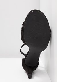 Chaussure à talon haut en suède noir avec une fine bride et une semelle texturée, affichant une finition lisse et un design moderne. Taille 37.