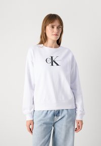 Sweatshirt blanc en mélange de coton, avec un col rond et des poignets côtelés. Logo Calvin Klein grisé au centre imprimé en gras.