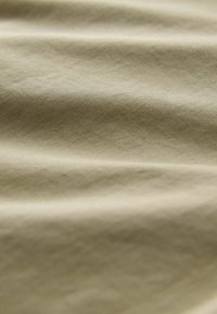 Tissu vert olive clair avec une texture lisse et un éclat subtil, présentant de douces draperies et plis dans le matériau.