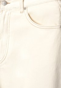 White denim fabric features visible stitching, a small front pocket, and a metal button closure at the waist.