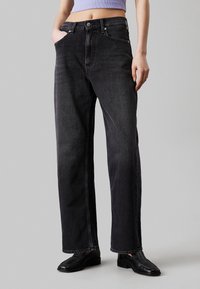 Jeans de mezclilla negra de pierna ancha con cintura alta, que cuentan con bolsillos frontales y una cremallera. El material tiene una textura suave y un ligero desgaste.