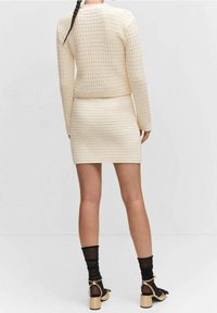 Ensemble en tricot couleur crème composé d'un pull et d'une mini-jupe, texturé avec un motif en grille. Associé à des chaussettes noires transparentes et des sandales beiges à talons blocs.