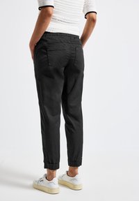 Pantaloni neri dalla vestibilità ampia con vita elasticizzata e caviglie a risvolto; due tasche sul retro; abbinati a sneaker bianche.