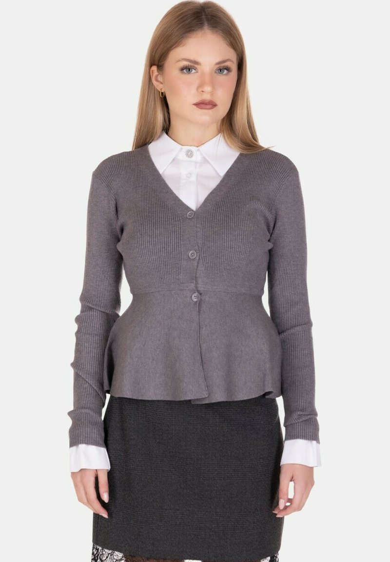 Cardigan grigio a coste con scollo a V, caratterizzato da un busto aderente e un orlo svasato, abbinato a una camicia bianca con colletto e una gonna scura.