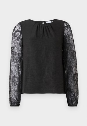 Zwart langemouwtop met een body van textuurstof en floral kantmouwen. Sluiting met keyhole aan de achterkant met een lus. Elegante uitstraling en gedetailleerde accenten.