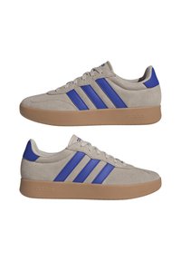 Sneakers in suede grigio con dettagli blu e tre strisce. Presentano una suola in gomma marrone, punta rotonda e chiusura con lacci.
