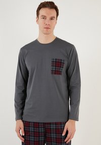 Camisa gris de manga larga con un bolsillo a cuadros rojos y negros, combinada con pantalones de cuadros en colores similares. Tejido suave, diseño informal.