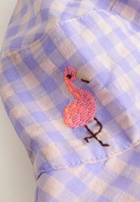 Ljuslila och krämfärgad ginghamtyg pryds av en pink broderad flamingodesign, med detaljerad stitching och kontrasterande bruna ben.
