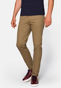 Khaki chinos o slim fit, z gładką teksturą i subtelnymi kieszeniami bocznymi, w połączeniu z burgundowymi trampkami o teksturowanym wykończeniu.