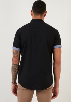 Zwarte T-shirt met korte mouwen en denim contrastmanchetten, gladde textuur, rechte zoom en subtiele achterkantnaaddetails.