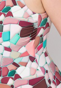 Maillot de bain coloré avec un motif en mosaïque de formes roses, teal et bordeaux. Fabriqué en tissu lisse avec un détail froncé sur le côté.