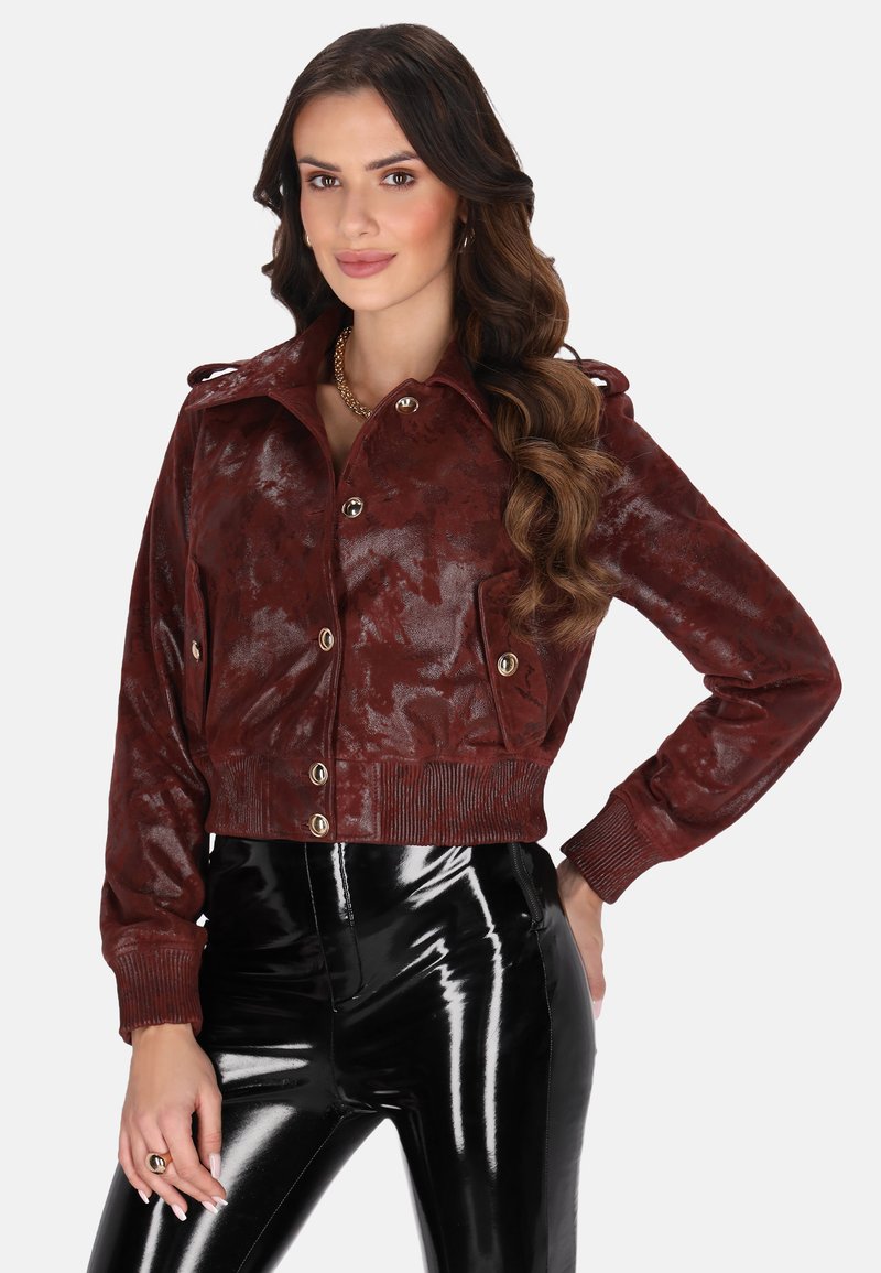 Zkrácená bordeaux bunda z lesklé ekokůže, s límečkem, předními knoflíky a pletenými manžetami, doplněná o černé lakované kalhoty.