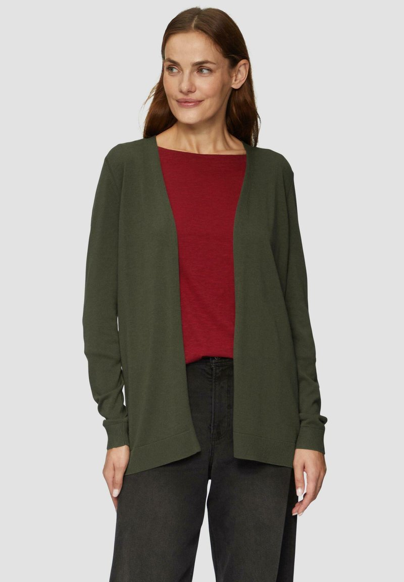 Olivgrüner Cardigan aus weichem Strickstoff, mit offenem Frontdesign, langen Ärmeln und lockerer Passform, über einem bordeauxfarbenen Oberteil getragen.