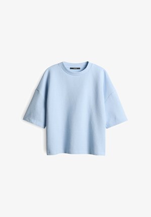 T-shirt oversized bleu clair en tissu texturé avec un col rond et des manches courtes. Présente une coupe décontractée et un design minimal.