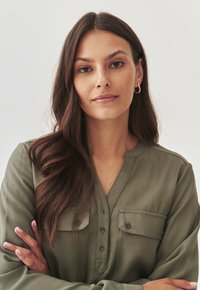 Olive green long-sleeve shirt with a V-neck, button closure, and two chest pockets. Soft texture and relaxed fit.