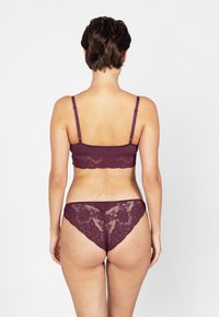 Burgunderfarbene Unterwäsche, bestehend aus einem Spitzen-Bralette mit verstellbaren Trägern und einem passenden Spitzen-Thong, der florale Muster zeigt.