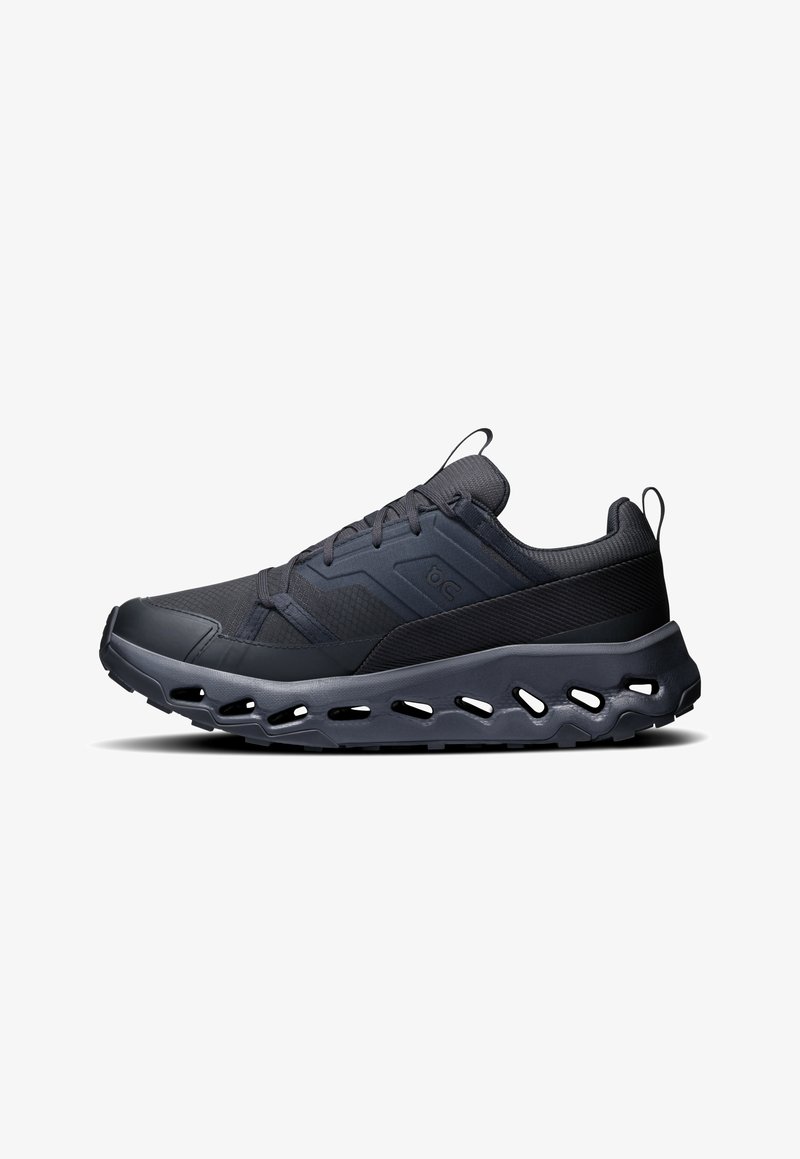 Zwarte sportschoenen met een gestructureerde mesh bovenkant, verheven accenten en een dikke, gevoerde zool met uitsparingen voor flexibiliteit en ventilatie.