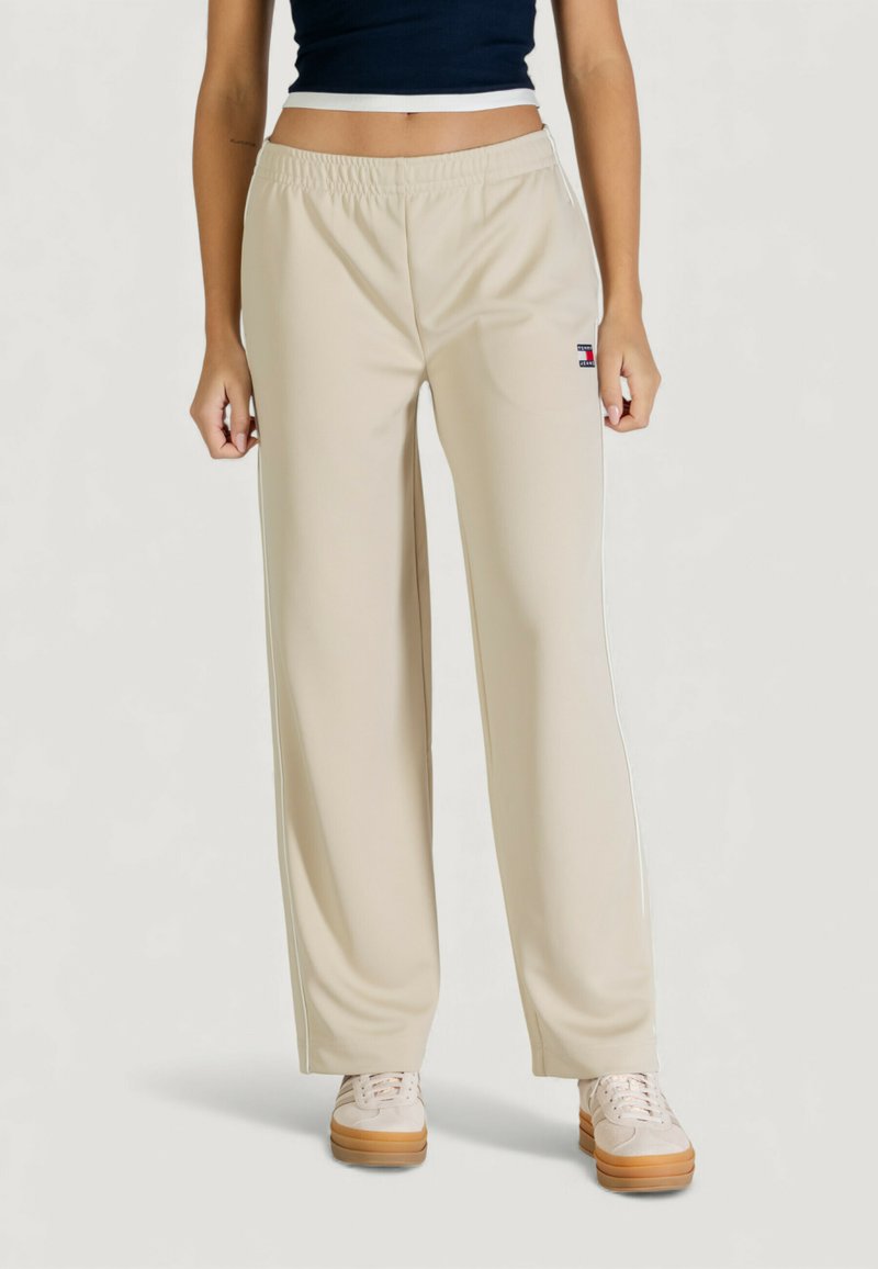 Pantaloni sportivi beige con vita elasticizzata, caratterizzati da strisce laterali e un piccolo logo. Realizzati in tessuto liscio e leggero.