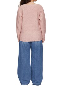 Lichtroze ribgebreide trui met een ronde halslijn, gedragen met ruime blauwe denim broek. Zachte textuur met wijde pijpen en omgeslagen zoom.